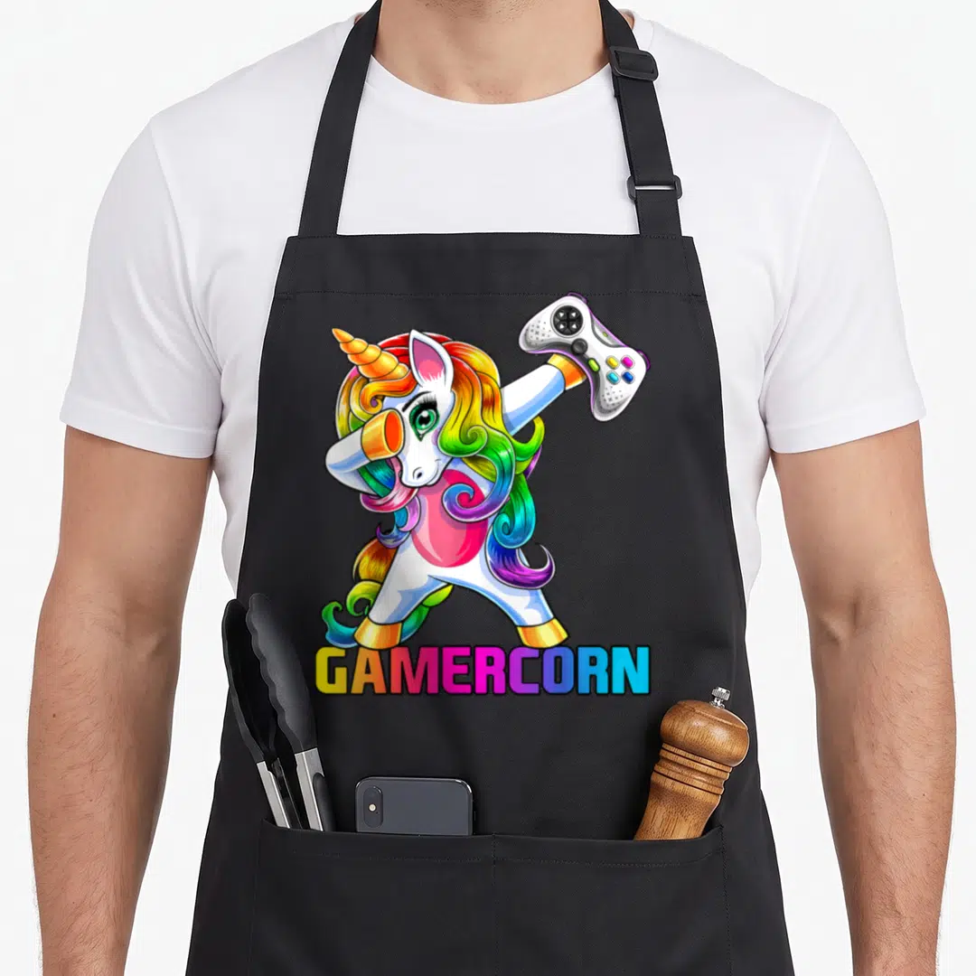Gamercorn video game apron - Cartoon unicorn dabbing holding game controller with rainbow GAMERCORN text — shown on a black cotton canvas apron against a white background