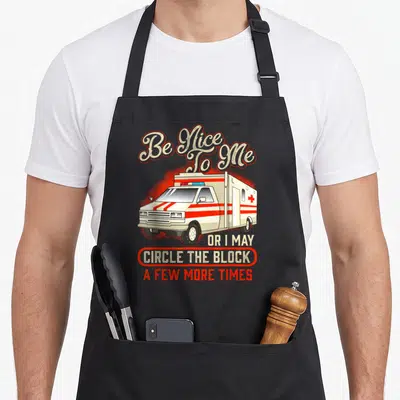 Amr emt apron - Cartoon ambulance with red stripes and text Be Nice To Me Or I May Circle The Block A Few More Times — shown on a black cotton canvas apron against a white background