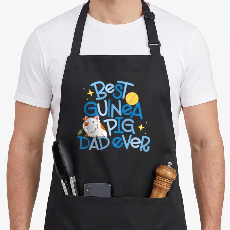 Miller crew apron - Cartoon guinea pig holding leaf next to stacked blue text Best Guinea Pig Dad Ever with yellow ball — shown on a black cotton canvas apron against a white background