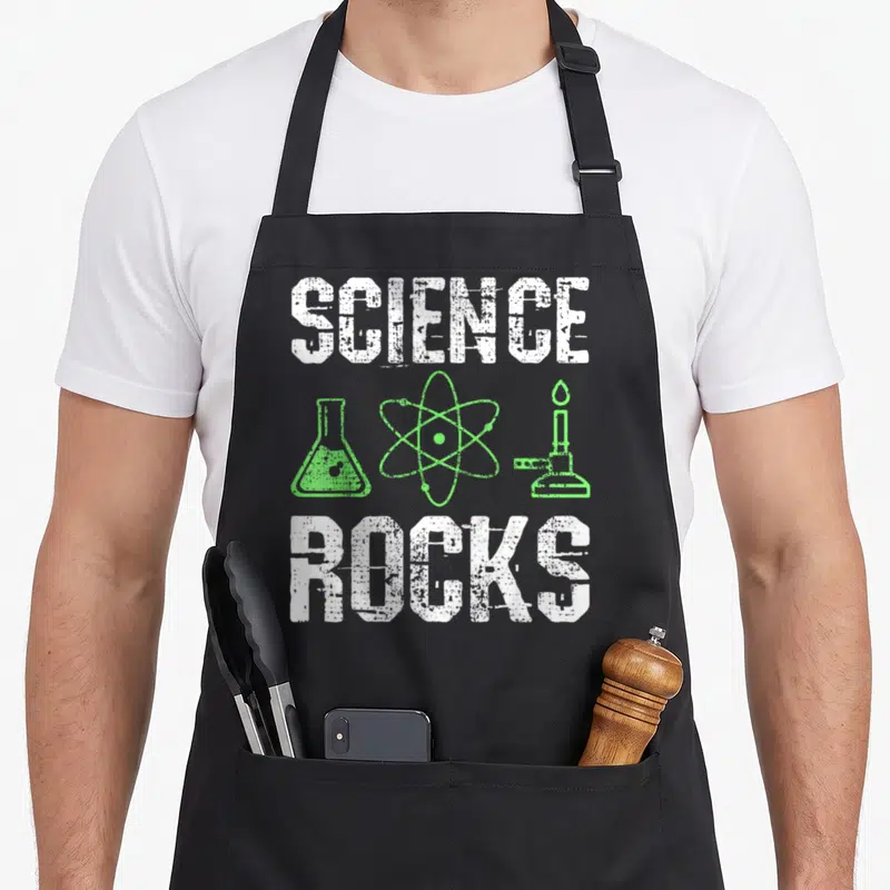 Rock chemistry apron - Distressed SCIENCE ROCKS text flanking green atom flask and bunsen burner icons — shown on a black cotton canvas apron against a white background