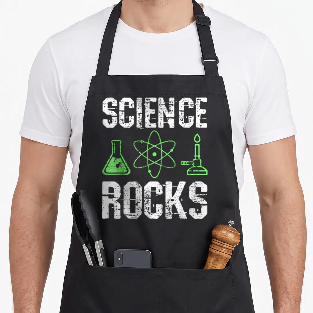 Rock chemistry apron - Distressed SCIENCE ROCKS text flanking green atom flask and bunsen burner icons — shown on a black cotton canvas apron against a white background