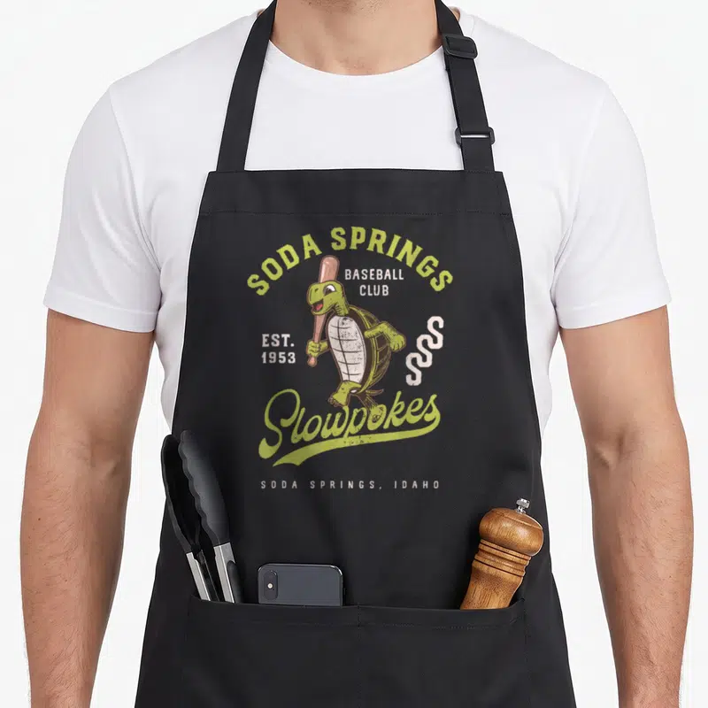 Soda spring apron - Cartoon turtle holding bat with Soda Springs Slowpokes text and EST 1953 — shown on a black cotton canvas apron against a white background