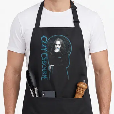 Ozzy patient apron - Blue vertical OZZY OSBOURNE text beside a grey line-art portrait with a blue halo — shown on a black cotton canvas apron against a white background