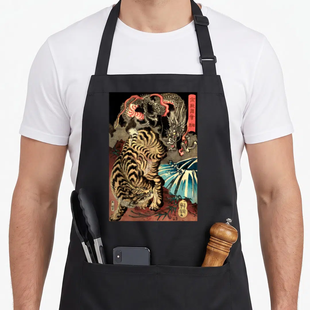 Fighting dragon apron - Japanese woodblock print of a tiger fighting a dragon with kanji text and blue water — shown on a black cotton canvas apron against a white background