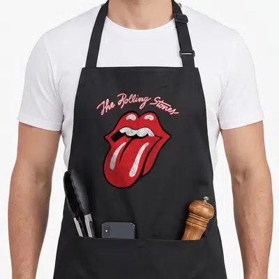 Funny script rolling stones apron - Arched script text above red lips and tongue with distressed texture — shown on a black cotton canvas apron against a white background