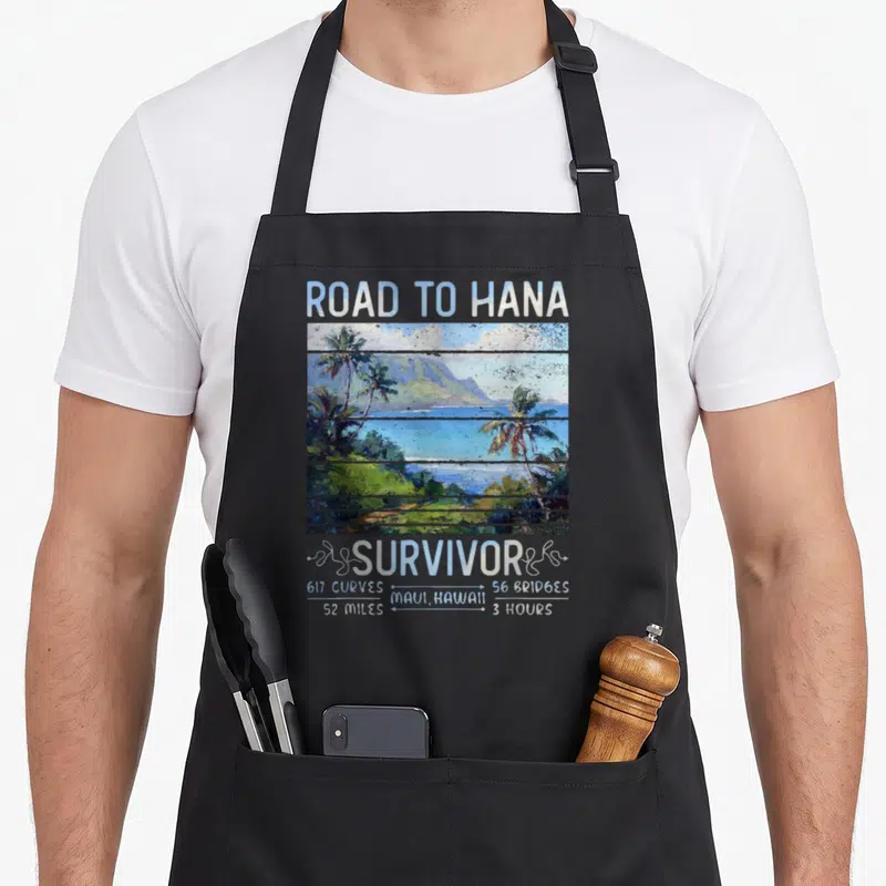 Rjc road apron - Road to Hana Survivor text above blue green landscape with 617 curves and 52 miles stats — shown on a black cotton canvas apron against a white background