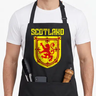 Funny scottish pride apron - Distressed yellow shield with red lion and SCOTLAND text — shown on a black cotton canvas apron against a white background