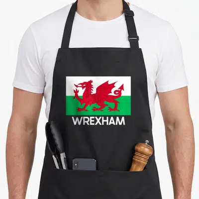 Flag welsh apron - Red dragon on white and green rectangle above white WREXHAM text — shown on a black cotton canvas apron against a white background