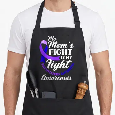 Fight arthritis awareness apron - Purple ribbon and white text reading My Mom's Fight Is My Fight Rheumatoid Arthritis — shown on a black cotton canvas apron against a white background