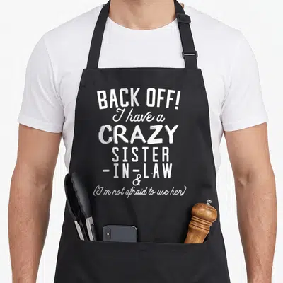 Law novelty apron - White stacked text reading Back Off I Have A Crazy Sister-in-Law sarcasm design — shown on a black cotton canvas apron against a white background