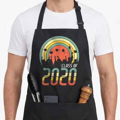 Class senior grad apron - Retro striped 2020 graphic with grey graduate silhouettes and cap toss against multi-colored — shown on a black cotton canvas apron against a white background