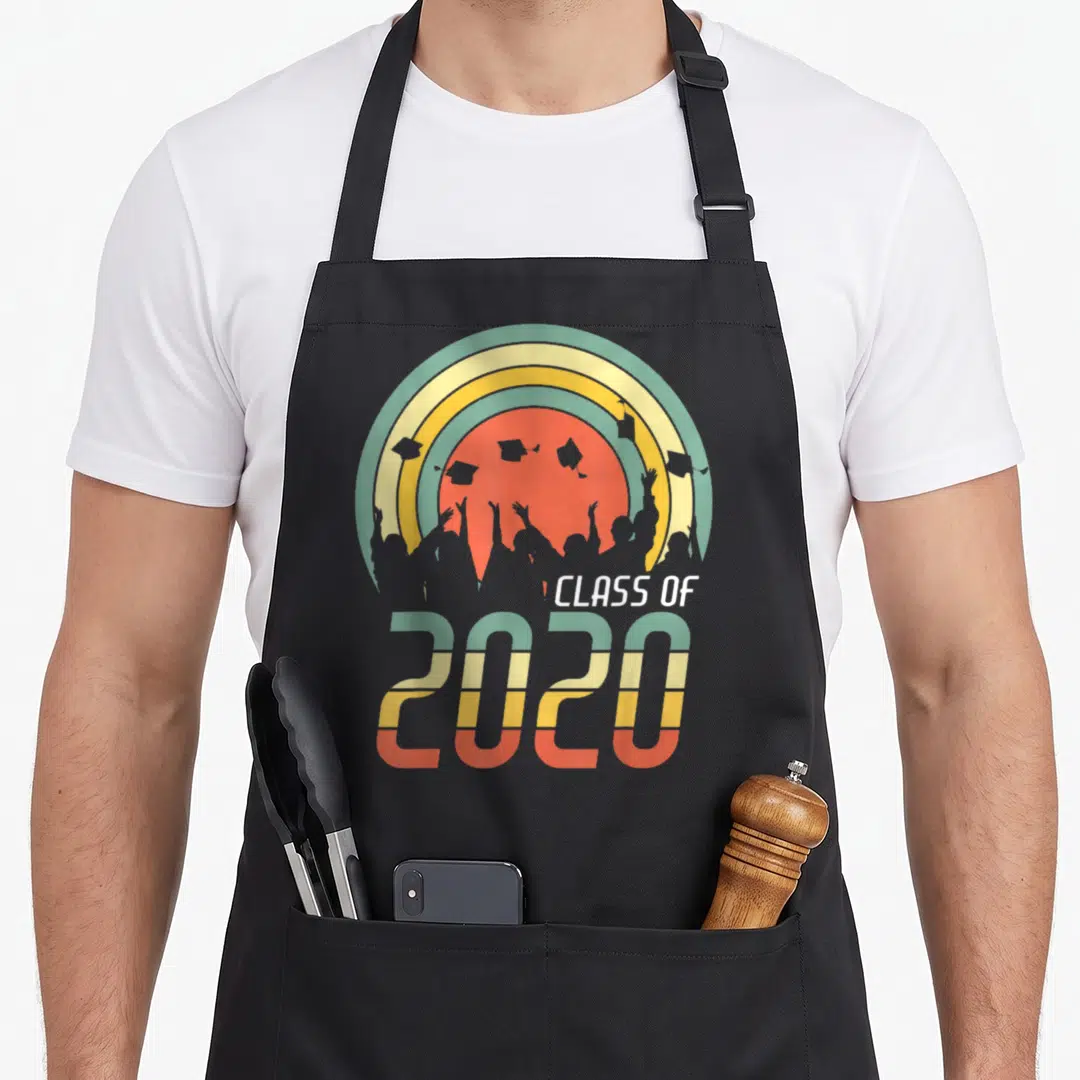 Class senior grad apron - Retro striped 2020 graphic with grey graduate silhouettes and cap toss against multi-colored — shown on a black cotton canvas apron against a white background