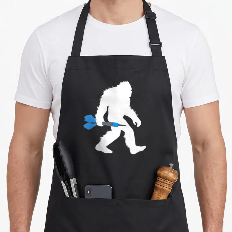 Dart bigfoot apron - White bigfoot silhouette walking right with blue and grey dart piercing midsection — shown on a black cotton canvas apron against a white background