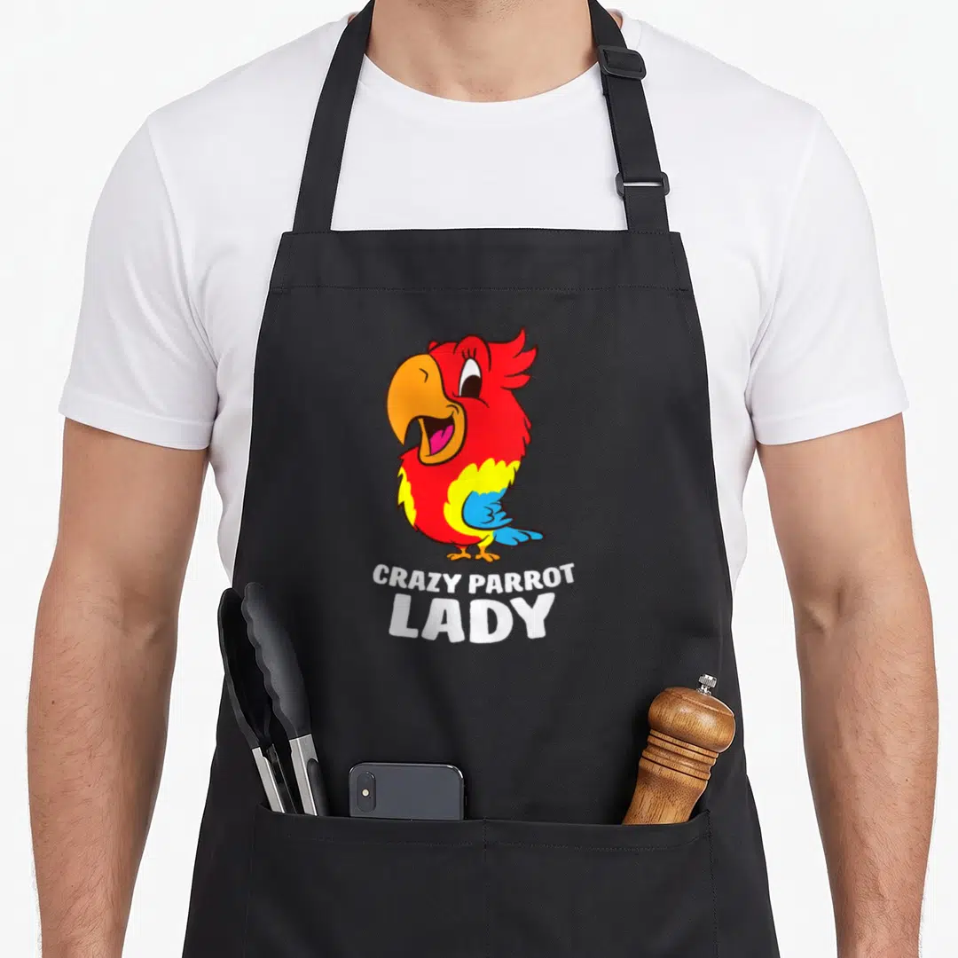 Obsessed parrot lady apron - Cartoon red parrot with yellow belly and blue wing above white text reading CRAZY PARROT — shown on a black cotton canvas apron against a white background