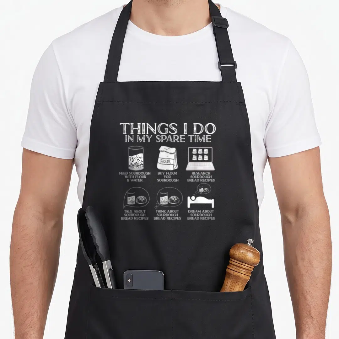 Spare bread apron - White line art showing feeding sourdough, buying flour, and dreaming about bread recipes — shown on a black cotton canvas apron against a white background