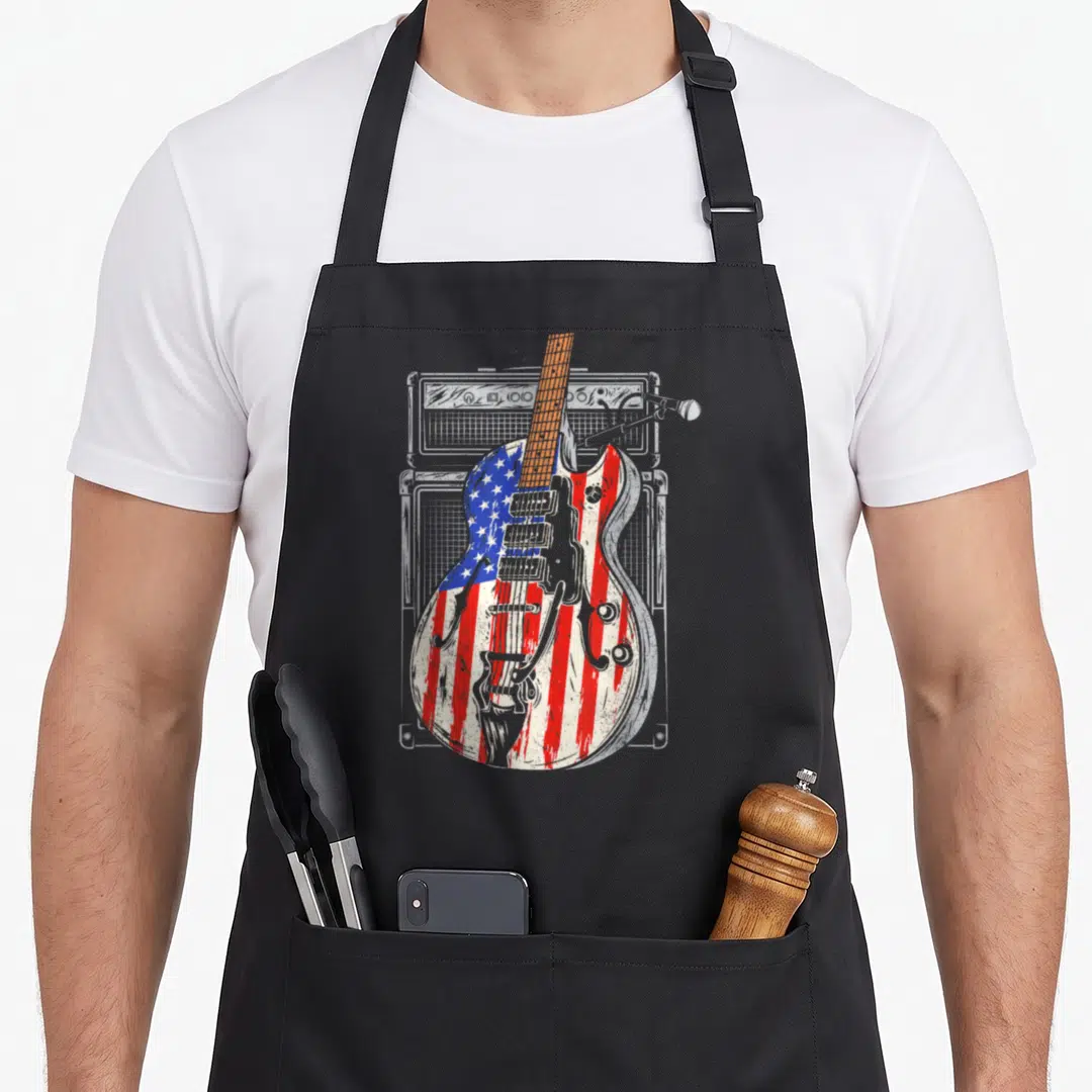 Flag cook's country aprons - Distressed electric guitar with red white blue flag pattern in front of grey amplifier — shown on a black cotton canvas apron against a white background