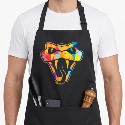 Snake colourful apron - Stylized snake head with open mouth filled with yellow, pink, blue, orange, and grey geometric — shown on a black cotton canvas apron against a white background