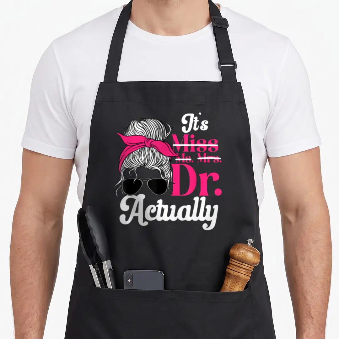 Graduate doctor apron - Cartoon messy bun with pink bandana and sunglasses next to stacked text crossing out Miss — shown on a black cotton canvas apron against a white background