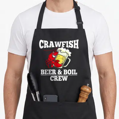 Beer crawfish boil apron - Red cartoon crawfish hugging a yellow beer mug under white arched CRAWFISH text — shown on a black cotton canvas apron against a white background