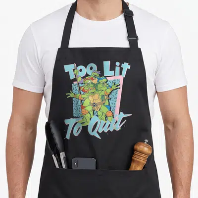 Lit teenage cooking aprons - Four green turtles clustered together with Too Lit To Quit text in blue and pink — shown on a black cotton canvas apron against a white background