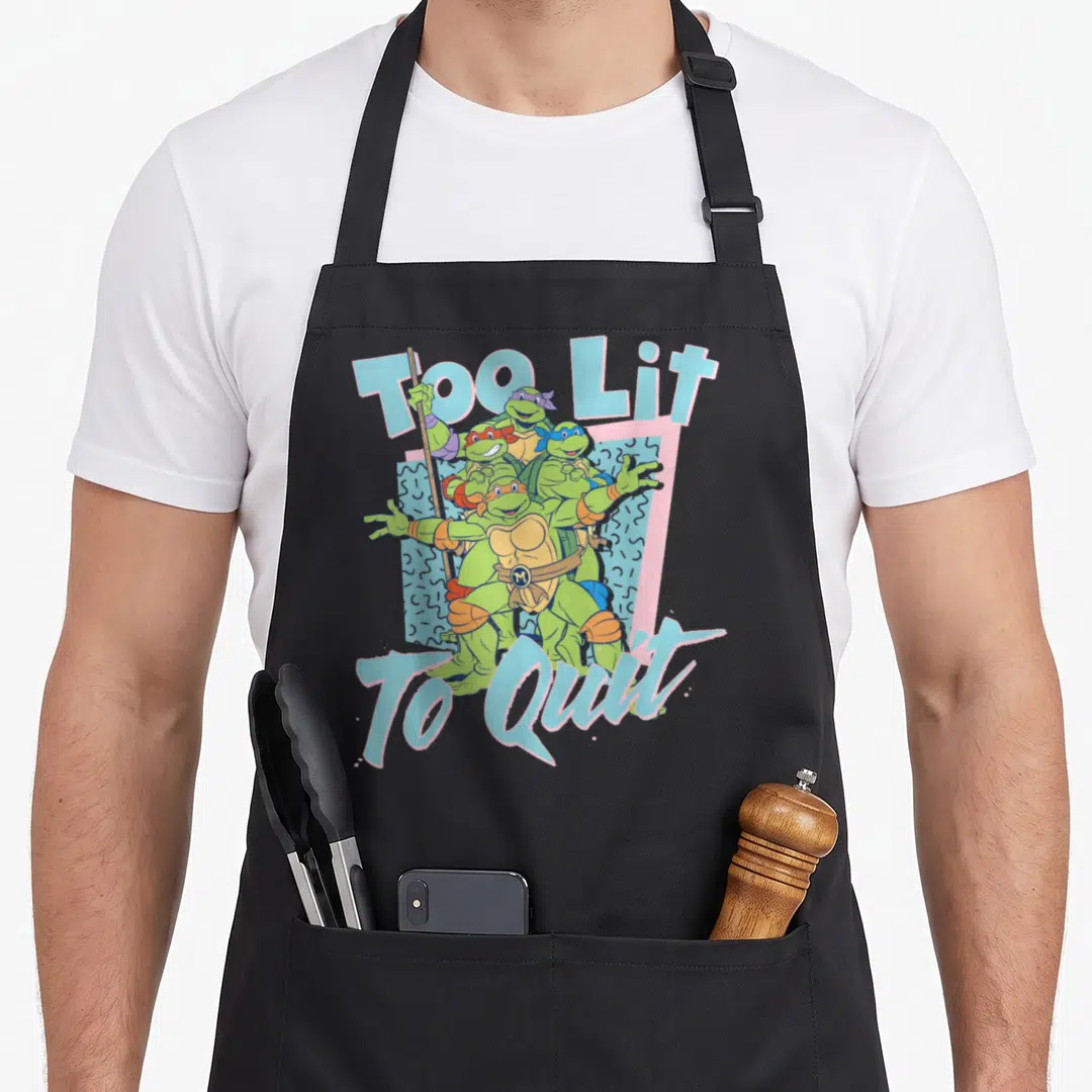 Lit teenage cooking aprons - Four green turtles clustered together with Too Lit To Quit text in blue and pink — shown on a black cotton canvas apron against a white background