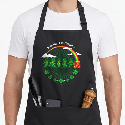 Grateful st patrick day aprons - Five green dancing bears walking toward a pot of gold under a rainbow with shamrocks — shown on a black cotton canvas apron against a white background