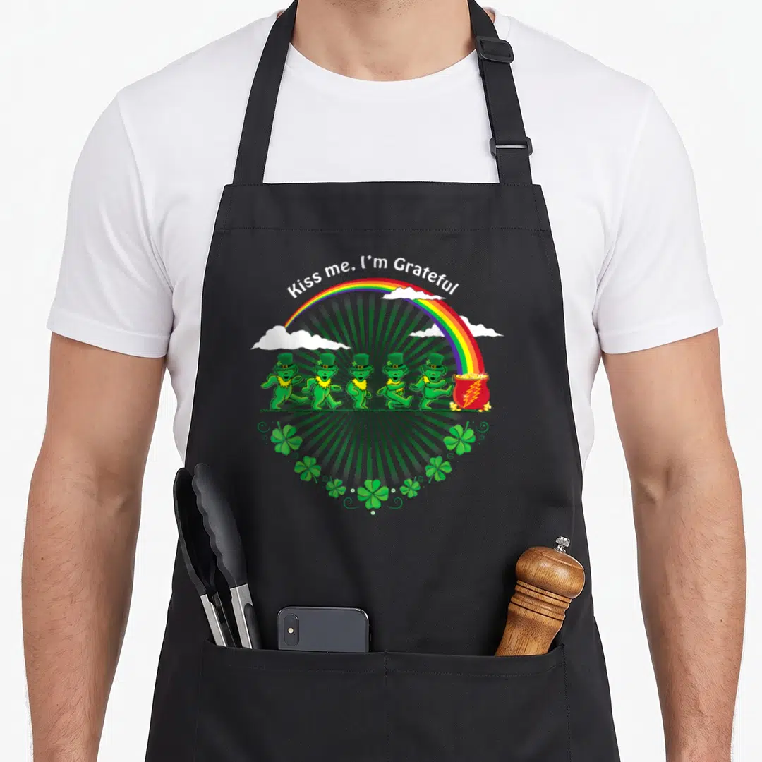 Grateful st patrick day aprons - Five green dancing bears walking toward a pot of gold under a rainbow with shamrocks — shown on a black cotton canvas apron against a white background