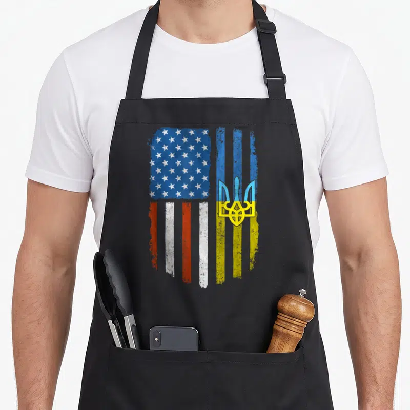 Root patriotic american flag apron - Distressed split US flag and Ukrainian trident design in blue white red and yellow — shown on a black cotton canvas apron against a white background