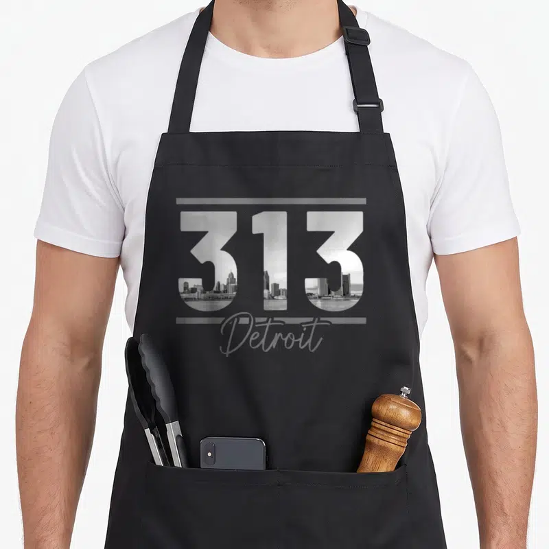 Code detroit apron - 313 filled with skyline photo, Detroit script, grey bars — shown on a black cotton canvas apron against a white background