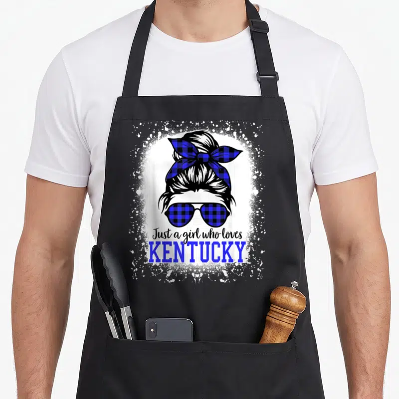 Kentucky messy aprons - Cartoon woman with blue plaid bun and sunglasses above Just a girl who loves KENTUCKY in white — shown on a black cotton canvas apron against a white background