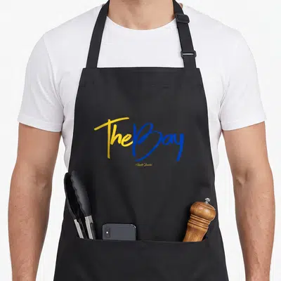 Bay curry apron - Yellow and blue script text The Bay Royally Branded stacked vertically — shown on a black cotton canvas apron against a white background