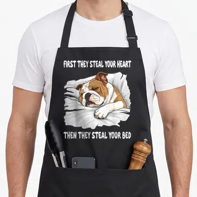 Sleeping english chef aprons - Cartoon bulldog sleeping on pillow with text first they steal your heart then they steal — shown on a black cotton canvas apron against a white background