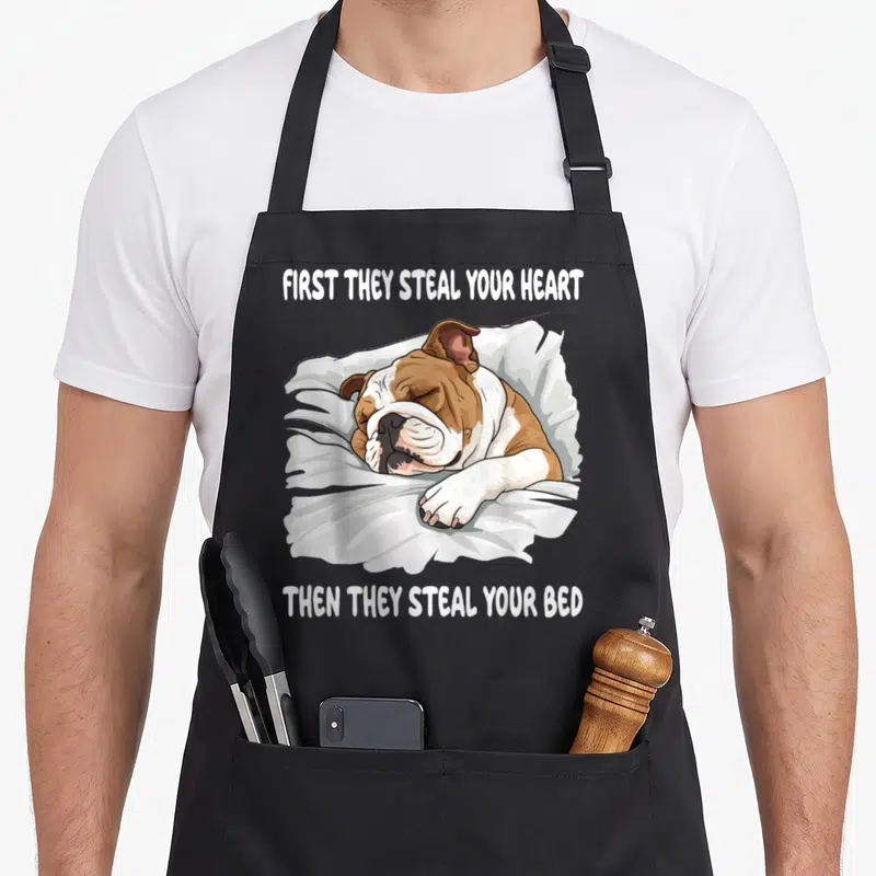 Sleeping english chef aprons - Cartoon bulldog sleeping on pillow with text first they steal your heart then they steal — shown on a black cotton canvas apron against a white background