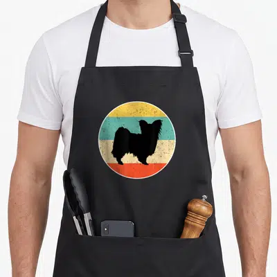 Vintage papillon dog apron - Black papillon dog silhouette inside a circle with yellow teal beige and red horizontal — shown on a black cotton canvas apron against a white background