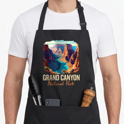 Grand outdoor apron - Retro Grand Canyon landscape illustration with orange and blue rocks and river above text — shown on a black cotton canvas apron against a white background