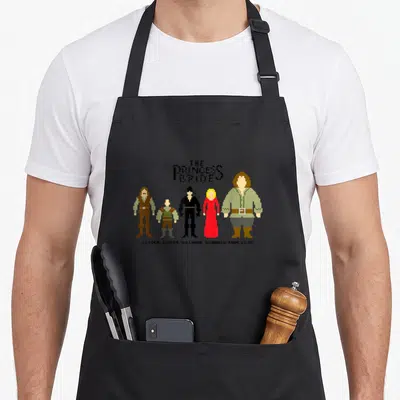 Bride princess apron - Pixel art lineup of Princess Bride characters with Heroes Giants Villains Wizards True Love text — shown on a black cotton canvas apron against a white background