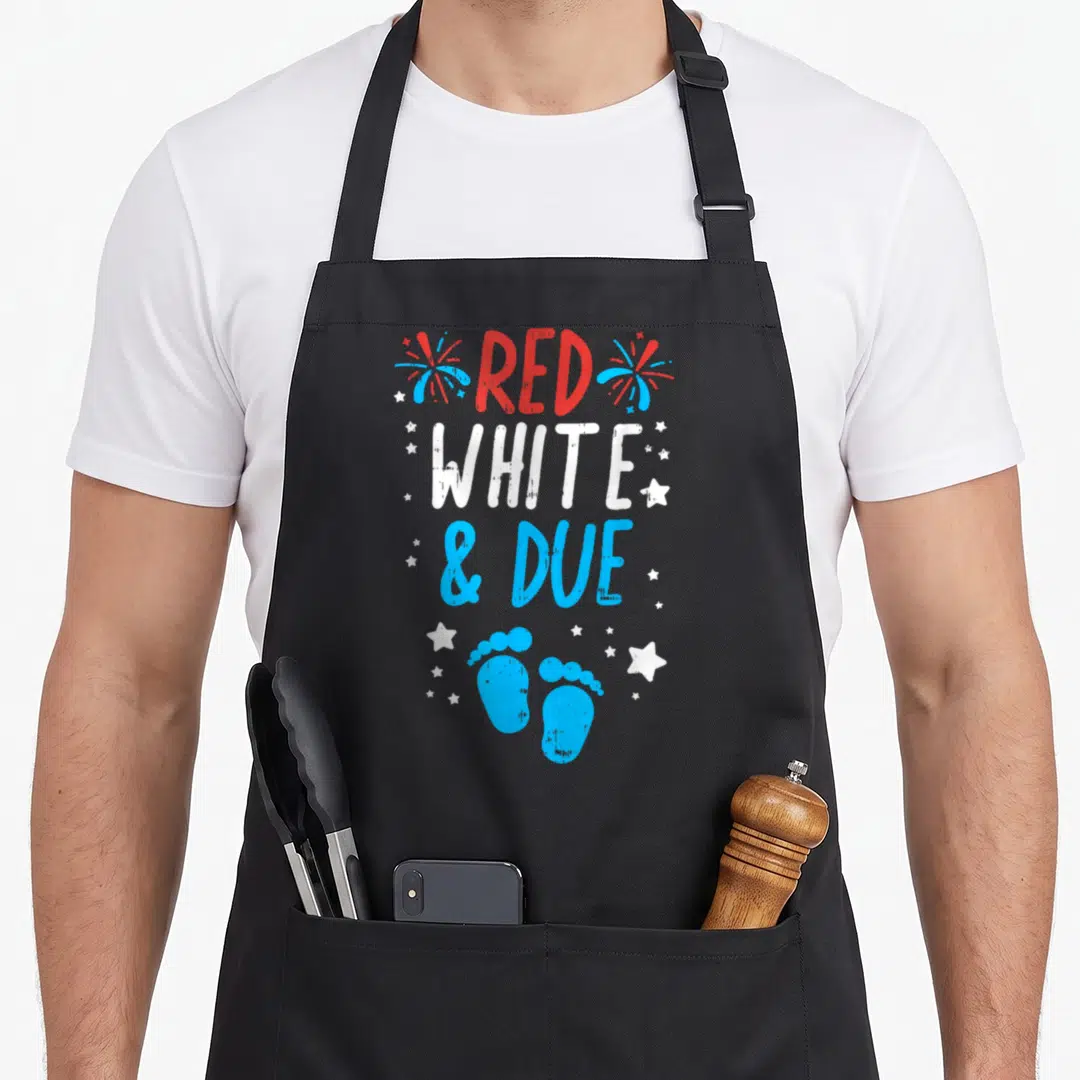 Shower 4th of july apron - Stacked Red White Due text with blue footprints, red and blue fireworks, and scattered white — shown on a black cotton canvas apron against a white background