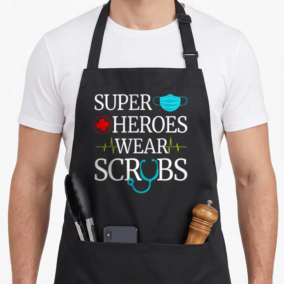 Heroe nursing apron - Stacked white text Super Heroes Wear Scrubs with blue mask red cross lime heartbeat — shown on a black cotton canvas apron against a white background