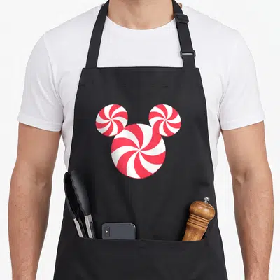 Icon holiday christmas aprons - Three red and white peppermint candies arranged in a head silhouette — shown on a black cotton canvas apron against a white background
