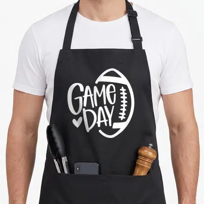 Season football team aprons - White GAME DAY text inside football outline with small heart — shown on a black cotton canvas apron against a white background