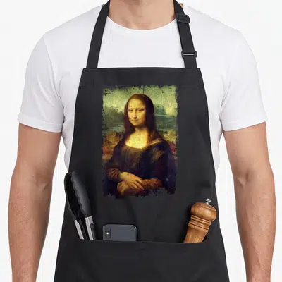 Lisa famous aprons - Distressed Mona Lisa portrait with torn edges in brown, green, yellow, and black — shown on a black cotton canvas apron against a white background