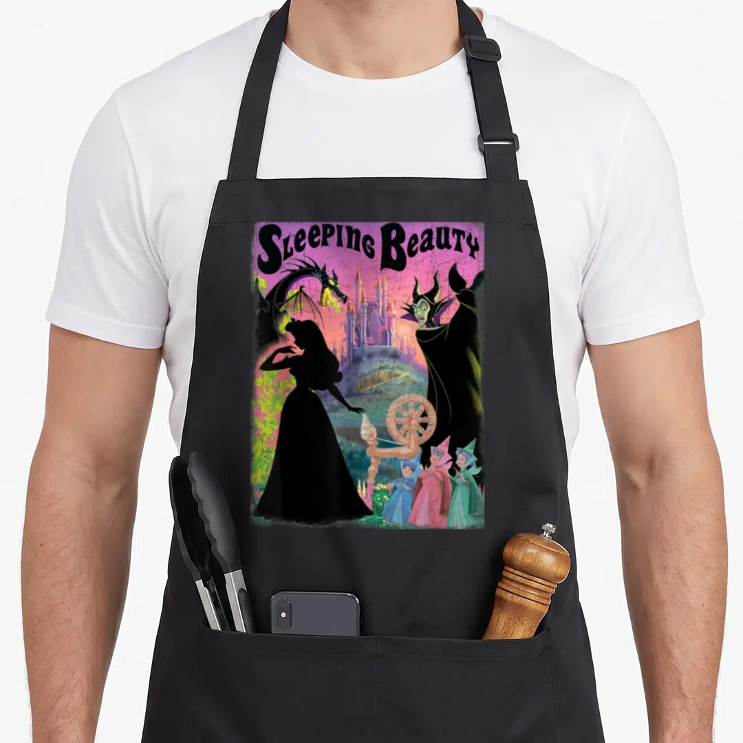 Aurora beauty apron - Sleeping Beauty text with Aurora silhouette, Maleficent, dragon, castle, spinning wheel — shown on a black cotton canvas apron against a white background