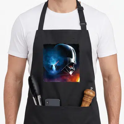 General apron with pockets - Darth Vader helmet profile reflecting two figures fighting with blue and red lightsabers — shown on a black cotton canvas apron against a white background