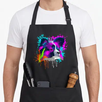 Splash papillon dog apron - Cartoon papillon head with purple magenta cyan orange and white paint splatters — shown on a black cotton canvas apron against a white background