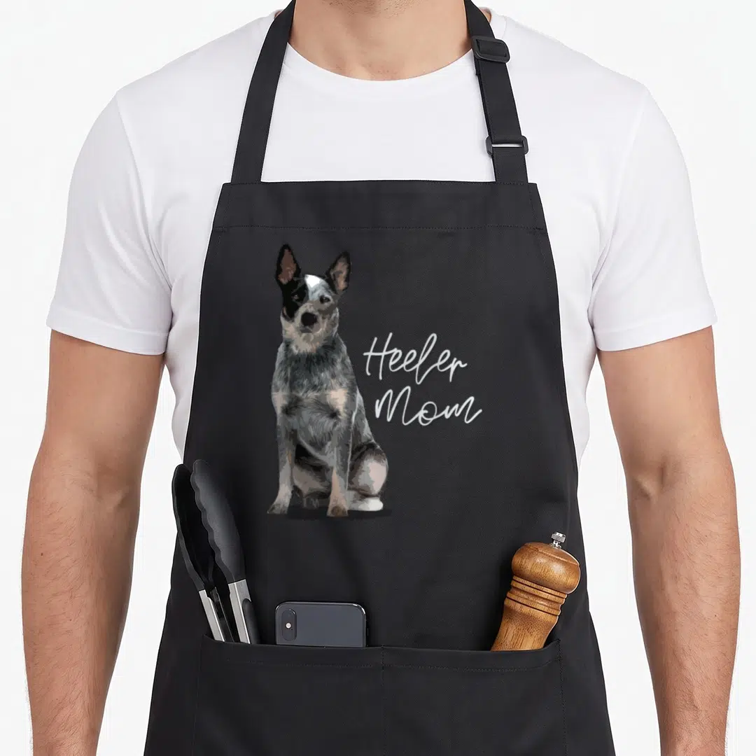 Domestic dog kitchen apron - Realistic dog in grey and black sitting beside Heeler Mom script text — shown on a black cotton canvas apron against a white background