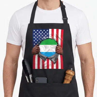 Proud sierra apron - Two hands rip USA flag revealing green white blue striped Sierra Leone flag — shown on a black cotton canvas apron against a white background