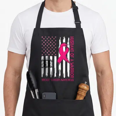 Husband warrior support breast cancer awareness aprons - Pink ribbon over distressed flag with husband of a warrior — shown on a black cotton canvas apron against a white background