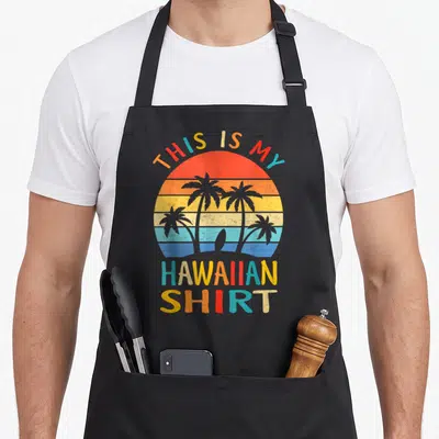 Tropical hawaiian apron - Retro striped sunset with four palm trees surfboard and text THIS IS MY HAWAIIAN SHIRT — shown on a black cotton canvas apron against a white background