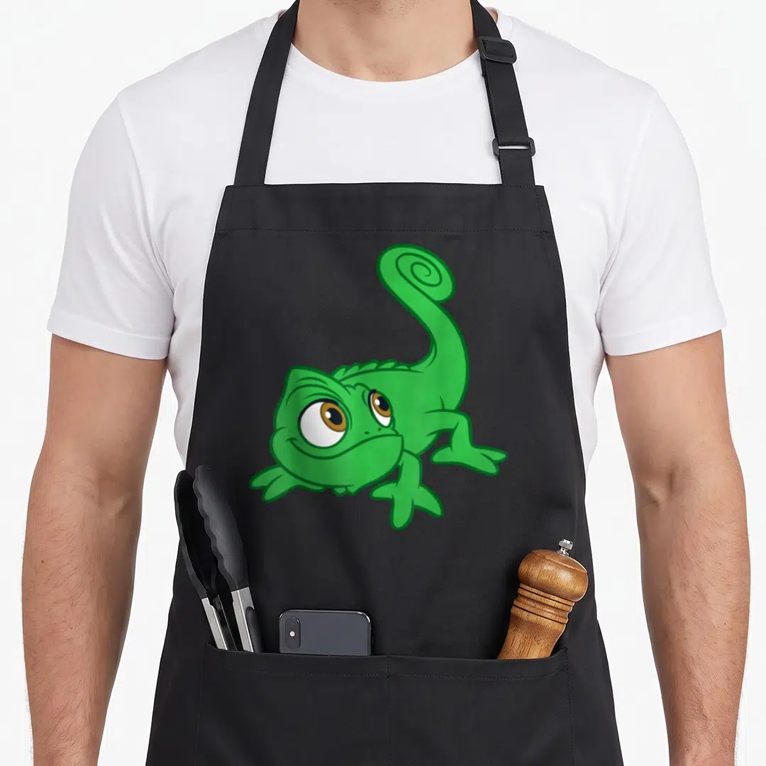 Pascal face apron - Green cartoon chameleon with large brown eyes and curled tail — shown on a black cotton canvas apron against a white background