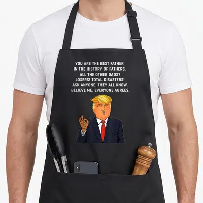 Donald disaster apron - Six lines of sarcastic text about fathers above a cartoon man in a suit making an okay gesture — shown on a black cotton canvas apron against a white background